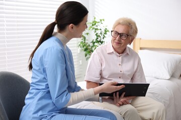 Obraz premium Nurse with clipboard examining senior woman indoors. Home health care service