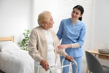 Fototapeta premium Nurse assisting senior woman with walking frame indoors. Home health care service