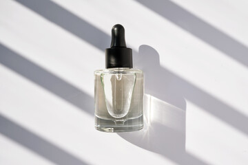 A bottle with a pipette with serum oil on a background with stripes of shadows.