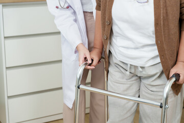 Orthopedic female doctor assists senior asian woman using walker for balance training, standing...