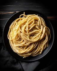 A top-down view of a gourmet pasta dish, arranged in a natural swirl on a dark plate. The scene is set with moody, dramatic lighting, creating a painterly, rustic still life.
