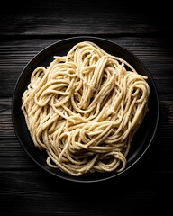A top-down view of a gourmet pasta dish, arranged in a natural swirl on a dark plate. The scene is set with moody, dramatic lighting, creating a painterly, rustic still life.