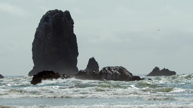 Ground level slow motion shot of waves crashing against Haystack Rock at Cannon Beach, Oregon on a sunny day.