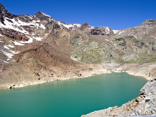Vivid turquoise lake reflecting rugged brown mountains in the Italian Alps.