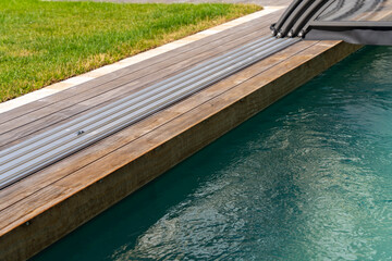 Vue d’une piscine couverte entourée d’un caillebotis en bois, intégrée harmonieusement dans un jardin paysager conçu par une entreprise spécialisée.