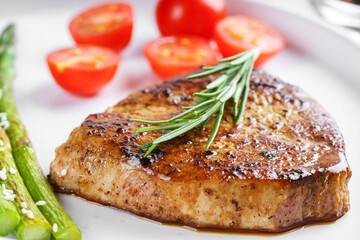 Close up, macro of tasty grilled beef steak served with green asparagus and cherry tomatoes on white plate, with cutlery. Perfect for food menu, diet, or culinary design concepts.