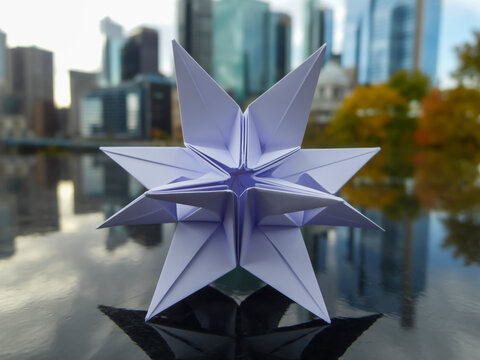 Delicate paper star sculpture reflects city skyline and autumn trees