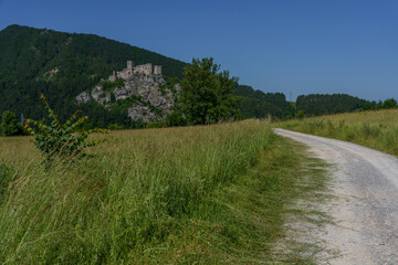 Gravel road through meadows with ruined castle on rocky hill