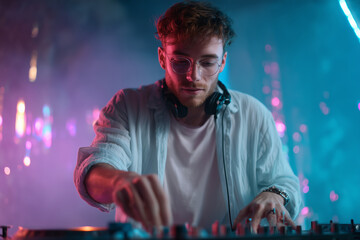 Young male DJ mixing music at a vibrant club with colorful neon lighting and smoke effects