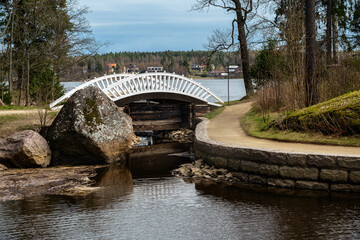 White arched bridge over a small channel and a sandy path leading to it in a city park.