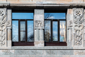 Two rectangular windows with brown frames against a wall of gray blocks with an ornament. From the Windows of the World series.