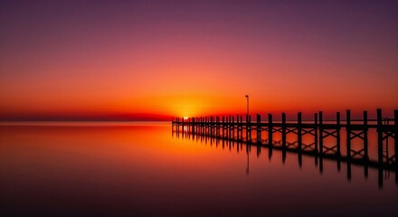 Stunning sunset over a calm ocean with a pier silhouette. Vibrant colors reflected in the water. Peaceful and romantic seascape for travel backgrounds or meditation concepts.