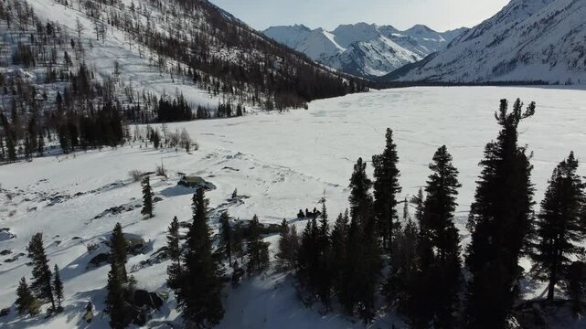 Drone aerial footage of a snowmobile riding across a frozen lake and snowy terrain in Russia. Captured from various angles, this footage highlights winter adventure, remote wilderness