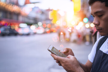 Young man holding smartphone and interacting with social media app, glowing emojis and location pin...
