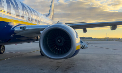 Plane on runway at sunset. Commercial aircraft with visible engine, wing and fuselage, symbolizing