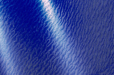 Water surface texture with blue waves and sunlight reflections. Calm liquid flow creating ripple