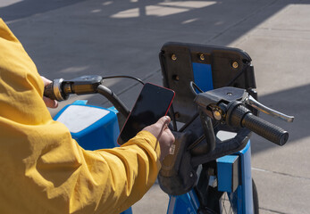 young man uses cell phone to unlock a public bike station bike
