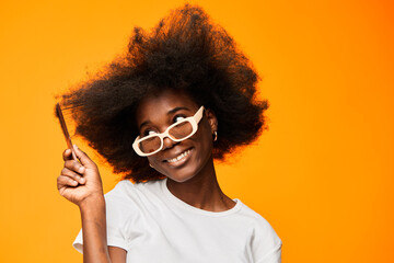 Happy young woman with natural afro hairstyle playfully combing her hair against a vibrant orange...