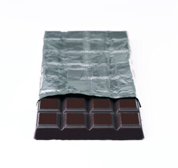 Dark chocolate bar partially wrapped in silver foil on white background