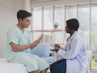 Caucasian man patient with woman doctor nurse carer physical therapist black people sit on bed talk helping support give advice holding hand arm for injury inside medical clinic hospital room service.
