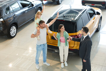 Salesman giving car key to happy family in salon