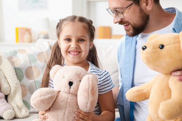 Father and his daughter playing with teddy bears on sofa at home