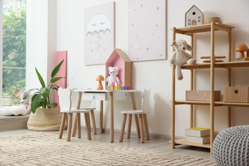 Contemporary furniture, toys and decor near white wall in stylish playroom. Interior design