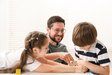 Father and his children playing with wooden figures at white table indoors