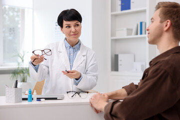 Fototapeta premium Ophthalmologist consulting young man at white table in clinic