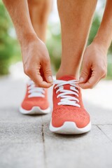 Athlete tying shoelaces on red running shoes before workout