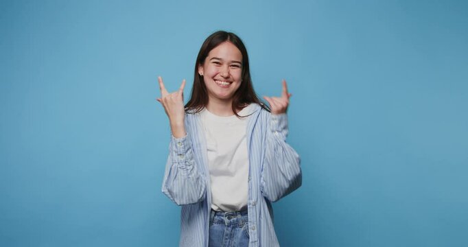 Smiling young woman showing hand rock gesture sign against a blue background in a cheerful indoor setting