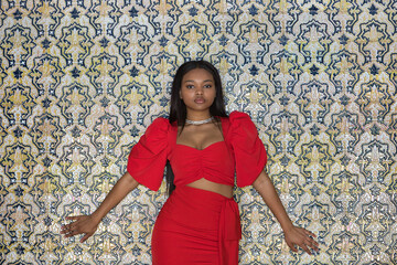 Young, beautiful, African woman in a red dress, posing as a model looking at the camera leaning...