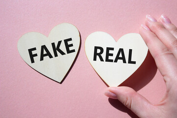 Real or Fake symbol. Concept word Real or Fake on wooden hearts. Beautiful pink background....