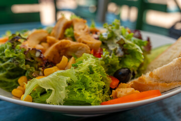 Fresh garden salad with grilled chicken, vibrant vegetables, and crusty bread at a sunny outdoor cafe