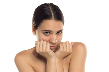 Studio shot of young woman looking shy with clenched hands under her chin, on white background.