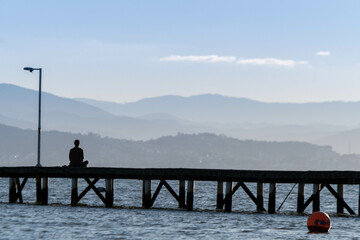 man meditating sitting on a pier by the sea