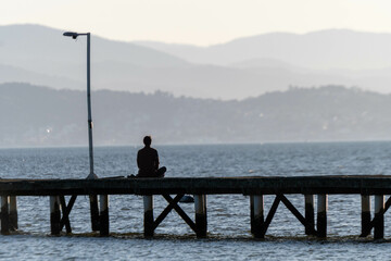 man meditating sitting on a pier by the sea