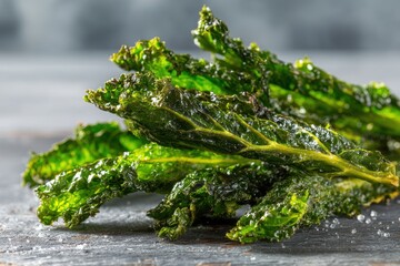 Close-up of crispy kale chips seasoned with sea salt, a healthy and delicious snack, displayed on a dark wooden surface with a blurred background.