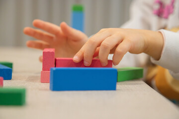 A young child plays indoors during the day, focusing intently while building a structure with colorful wooden blocks, developing fine motor skills, creativity, and early cognitive abilities.