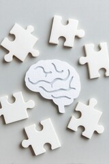 White jigsaw puzzle pieces surrounding paper brain on gray background