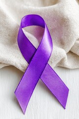 Purple awareness ribbon lying on white wooden background with beige cloth