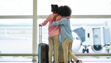 Two children hugging with luggage at airport terminal window