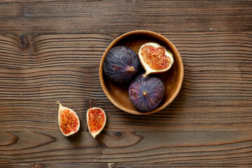 Purple ripe figs in a wooden bowl top view on a wooden background