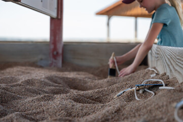 Child brushing away sand at a dinosaur fossil dig exhibit. 