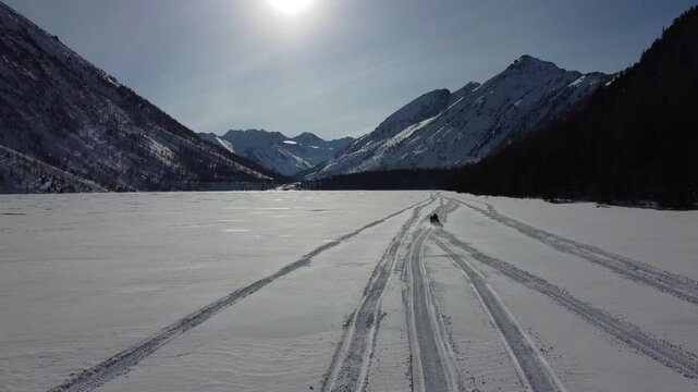 Drone aerial footage of a snowmobile riding across a frozen lake and snowy terrain in Russia. Captured from various angles, this footage highlights winter adventure, remote wilderness