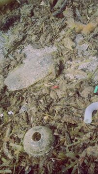 Vertical video, Panorama rock-sand seabed covered with plastic trash and oter debris, Closeup, Slow motion. Concept plastic pollution of Ocean 