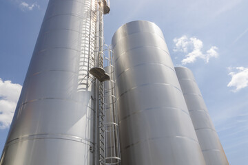 Stainless steel milk silos at a dairy processing plant under a bright blue sky.
