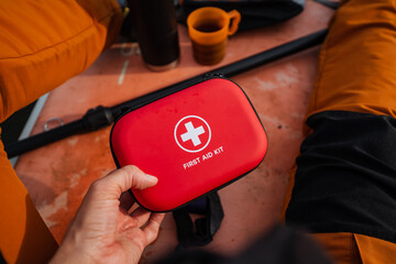 A person is firmly gripping a bright red first aid kit in their hands, fully prepared for any sort...