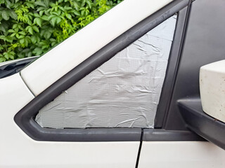 Car with broken window covered with packing tape and plastic foil parked