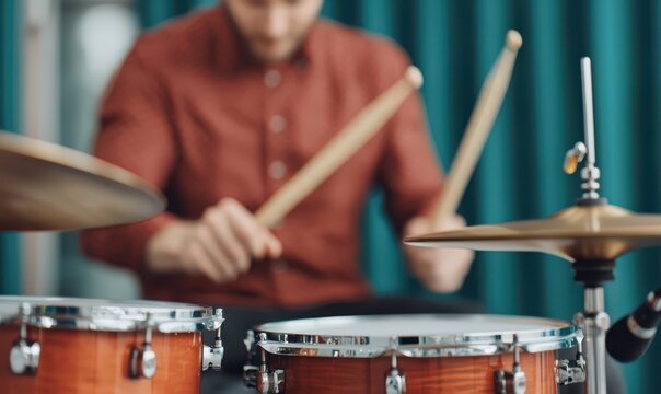 A focused image of a person playing a drum set with drumsticks in motion, highlighting the drums and cymbals in a music studio setting.